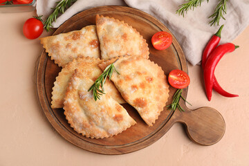 Wooden board with baked meat empanadas, vegetables and rosemary on color background