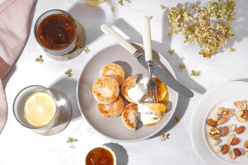 Composition with tasty cottage cheese pancakes, glass of water, coffee and nuts on light background