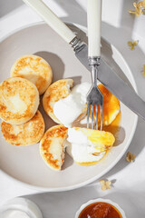 Plate of tasty cottage cheese pancakes with sour cream and jam on light table, closeup