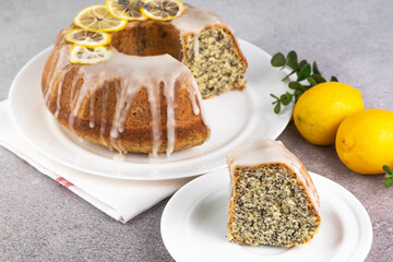 Lemon poppy seed Bundt Cake with icing and in a plate and a slice on a gray table.