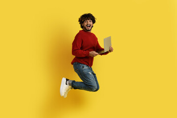 Happy indian man jumping in the air with laptop