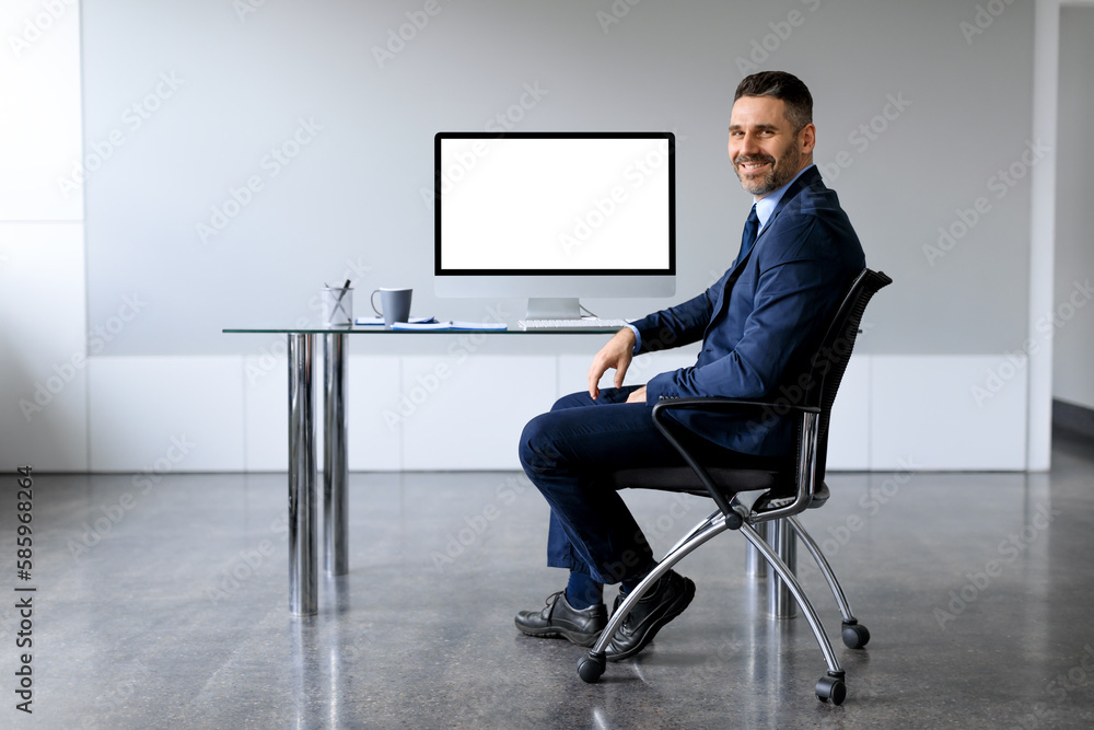 Poster happy middle aged businessman sitting on desk with computer with empty blank screen at office, free 