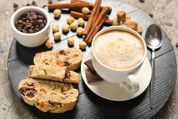 Board with delicious biscotti cookies, cup of coffee, hazelnuts and cinnamon on grey grunge background
