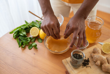 Making kombucha tea drink at home, fermented drink flavoured with ginger, lemon and mint. Healthy drink, organic probiotic beverage. Black young male hands holding kombucha scoby.