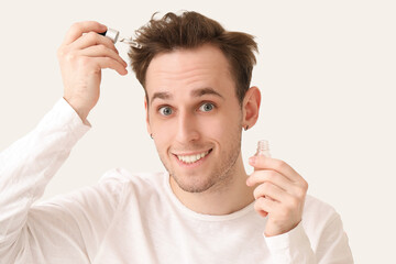 Young man with serum for hair growth on white background, closeup