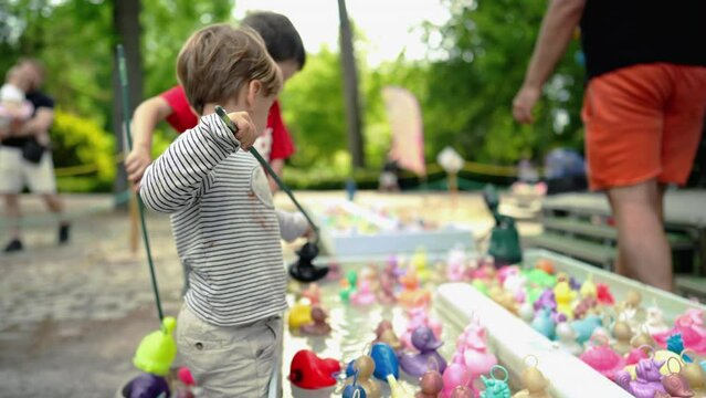 Children fishing plastic ducks at amusement park. child holding fishing rod having fun at funfair festival party