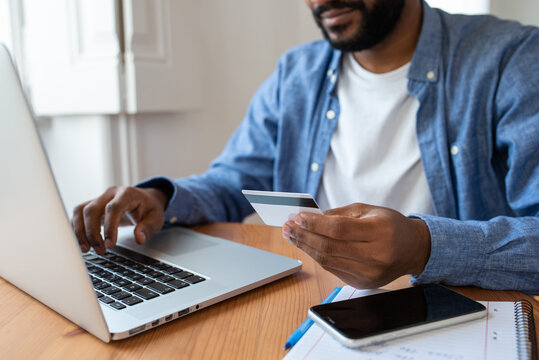 Close up of a young black man buying online in his living room with laptop, holding his bank card