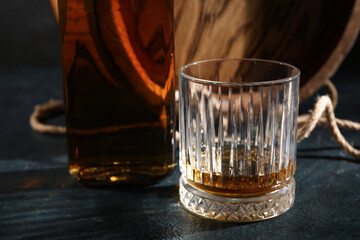 Glass and bottle of tasty whiskey on dark background