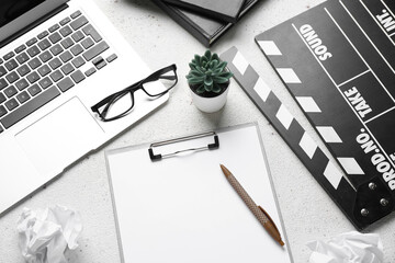 Clipboard with movie clapper, plant, eyeglasses and laptop on white background