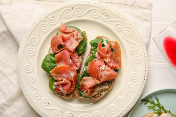 Plate of tasty bruschettas with ham on white table