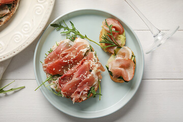 Plate of tasty bruschettas with ham on white wooden background