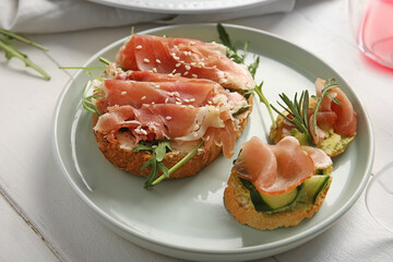 Plate of tasty bruschettas with ham on white wooden background