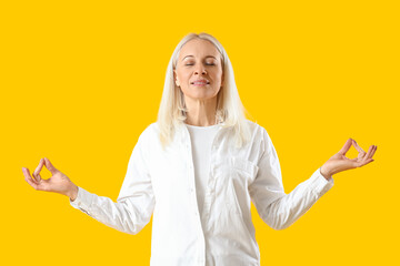 Mature woman meditating on yellow background