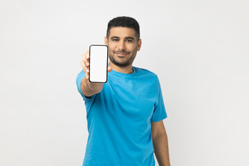 Cheerful satisfied man holding out smart phone with empty screen, copy space for advertisement.