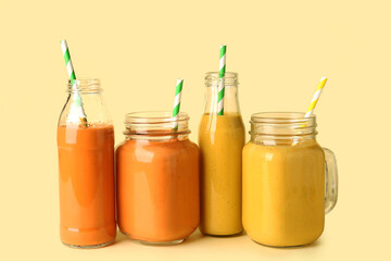 Glasses and bottles of different tasty smoothie with straws on yellow background