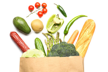 Paper bag with vegetables, bread and sausage on white background