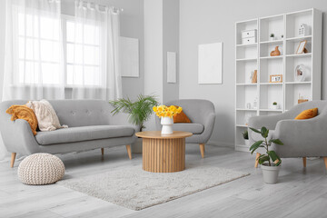 Interior of light living room with cozy sofa, armchairs and flower vase on coffee table