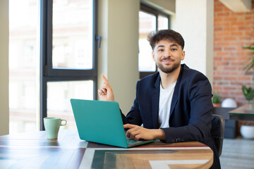young handsome man smiling cheerfully, feeling happy and pointing to the side. freelance concept with laptop
