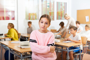 Portrait of sad young girl standing in classroom during lesson in school..