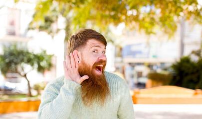 red hair bearded man looking happy, listening, trying to hear a secret conversation or gossip,...