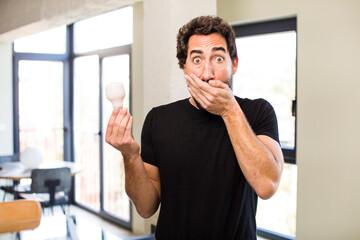 young crazy bearded covering mouth with a hand and shocked or surprised expression with a light bulb