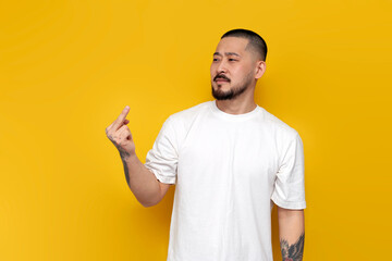 adult rude tattooed asian man in white t-shirt showing middle finger on yellow isolated background - Powered by Adobe