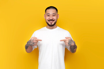 adult tattooed asian man in white t-shirt points to himself on yellow isolated background, korean...