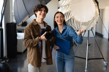 Young male photographer talking with female art director, preparing for photo shooting, standing near lighting equipment