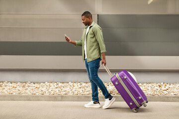 Black Traveler Man Using Cellphone Walking With Travel Suitcase Outside