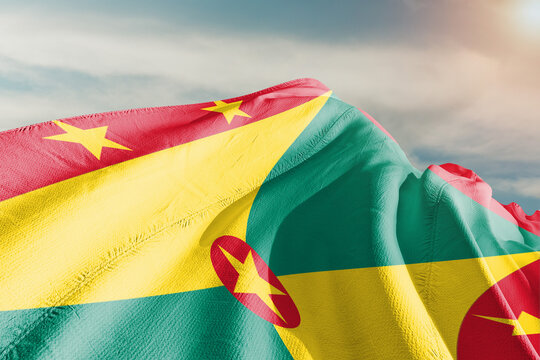Grenada national flag cloth fabric waving on beautiful grey sky. - Powered by Adobe