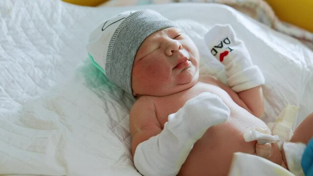Sweet new born baby in a cap and mittens. Nurse&rsquo;s gloved hands changing a diaper to a Caucasian infant. Close up.