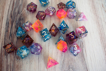 Many different dice scattered on a wooden table, view from above