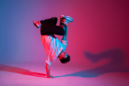 dancer doing acrobatic trick and dancing breakdance in neon red and blue lighting