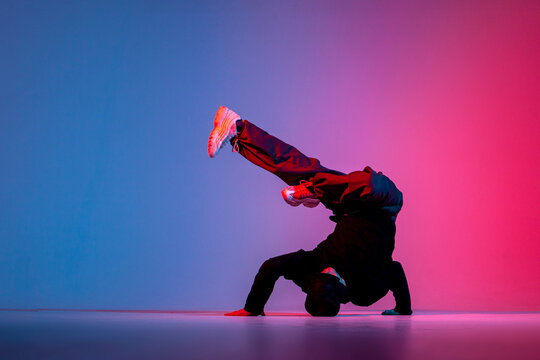 dancer doing acrobatic trick and dancing breakdance in neon red and blue lighting