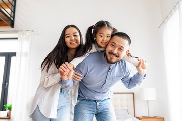 happy Asian family with a little daughter stand at home and rejoice, mom and dad hold the child in their arms and smile