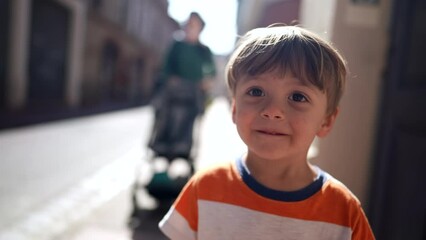 One small boy walking in city sidewalk. Child walks outdoors in urban street during sunny day. 2 year old kid walks outside