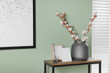 Branches with white fluffy cotton flowers on console table in cozy room. Interior design
