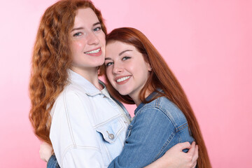 Portrait of beautiful young redhead sisters on pink background