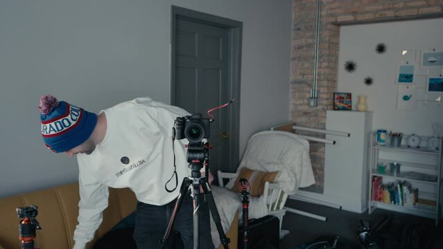 camera operator videographer sets wireless microphone reciever on hot shoe-top of camera. Caucasian aduld man is smiling while is setting up the equipment for a videoshoot. Red headphones-black tripod