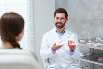 Fototapeta premium Doctor with educational model of dental implant consulting patient in clinic