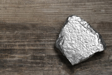 One silver nugget on wooden table, top view. Space for text