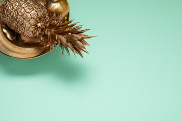 Golden bowl with fruits on turquoise background, top view. Space for text