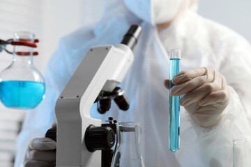 Fototapeta premium Scientist with test tube of light blue liquid and microscope in laboratory, closeup