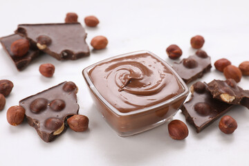 Bowl with tasty paste, chocolate pieces and nuts on white table
