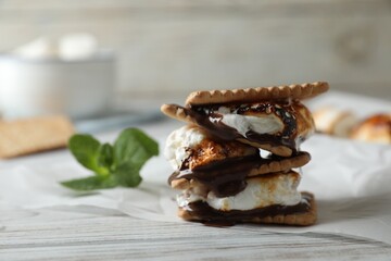 Delicious marshmallow sandwich with cracker and chocolate on white wooden table, closeup. Space for text