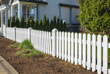Nice new wooden fence around house. Wooden white picket fence with green lawn. Street photo