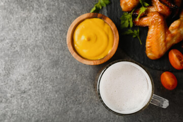 Mug with beer, delicious baked chicken wings and sauce on grey table, flat lay. Space for text