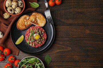 Tasty beef steak tartare served with quail egg and other accompaniments on wooden table, flat lay....
