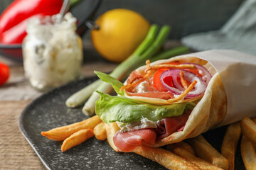 Delicious pita wrap with prosciutto, vegetables and potato fries on wooden table, closeup