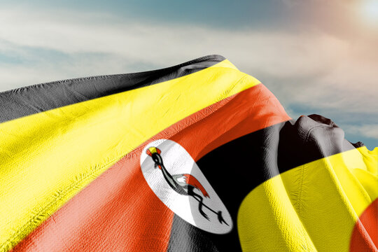 Uganda national flag cloth fabric waving on beautiful grey sky.
